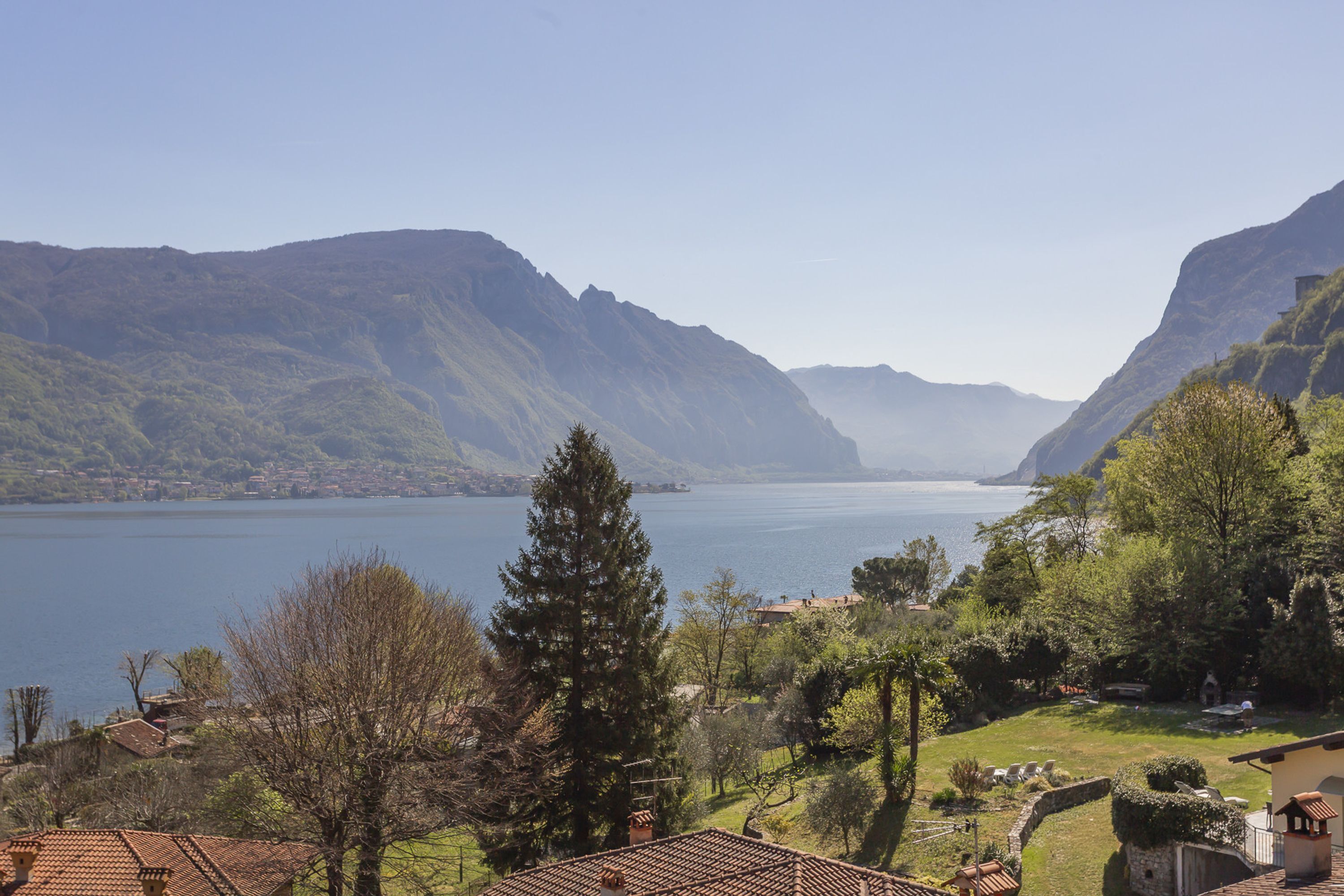Un paisaje montañoso con un lago, casas escalonadas y abundante vegetación.