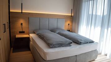 A modern bedroom with a large bed, bedside tables, and a headboard with integrated lighting.