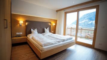 Quarto com cama de madeira, mesas de cabeceira, uma janela grande com vista para uma montanha nevada e uma varanda.