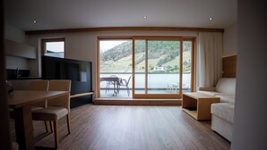 Un amplio salón con un gran ventanal corredera que da a un balcón, un comedor con mesa y sillas, y un sofá.