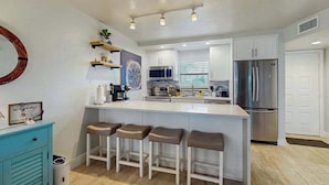 Una cocina moderna con una isla central, taburetes de bar, microondas, refrigerador y cafetera.