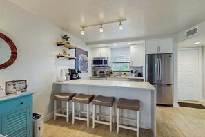 A modern kitchen with a central island, bar stools, a microwave, refrigerator, and a coffee maker. - Third-Floor Condo with Shared Outdoor Pool, Hot Tub, Tennis, W/D, and Free WiFi (Marco Island)