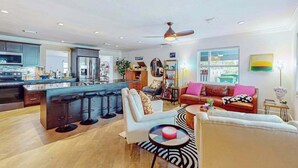 Een moderne keuken met een centraal eiland, een eetgedeelte met barstoelen, een woonkamer met een bank en een salontafel, en een groot raam met uitzicht.