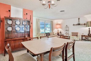 Ein Esszimmer mit großem Tisch, Stühlen, einer Vitrine und einer Couch, darüber ein Kronleuchter.
