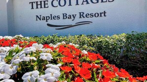 En skylt med texten ”The Cottages” vid Naples Bay Resort, omgiven av en blommig ram.