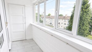 Ein Zimmer mit weißer Tür, einem Fenster mit Blick auf Wohnhäuser und einem Fliesenboden.