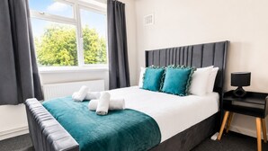 Ein ordentlich bezogenes Bett mit einer türkisblauen Tagesdecke, weißen Kissen und aufgerollten Handtüchern.