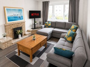A living room with a fireplace, a sofa set, a coffee table, and a television displaying 'NETFLIX'. - Stunning 2-bedroom apartment in charming Newport perfect for relaxing stay (Newport)