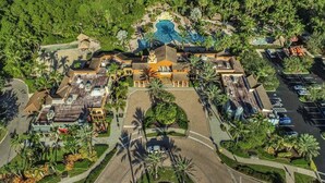 Vista aerea di un resort con un edificio centrale, diverse piscine e vegetazione lussureggiante.