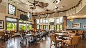 Un'ampia sala da pranzo con diversi tavoli e sedie, ampie finestre, ventilatori a soffitto e un lampadario.