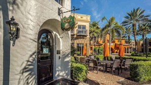 Un edificio con un cartello che riporta 'The Pub', posti a sedere all'aperto con tavoli e sedie, e palme sullo sfondo.