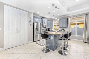 Een moderne keuken met roestvrijstalen apparatuur, een centraal eiland met barstoelen en een groot raam met gordijnen.