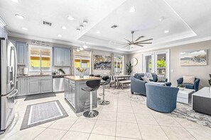 Een moderne keuken met een centraal kookeiland, barstoelen en een zithoek met een bank en salontafel.