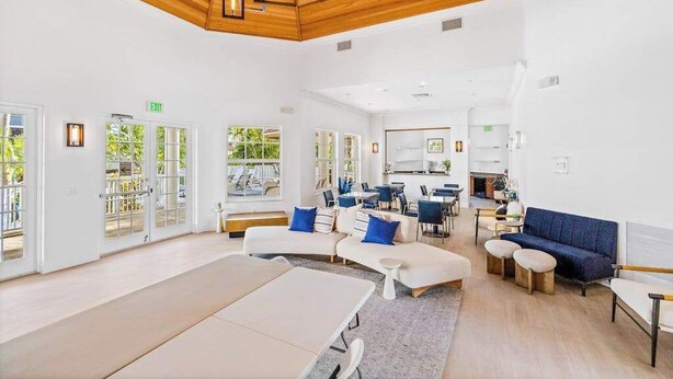 A spacious indoor area with a wooden ceiling, white walls, and a mix of seating arrangements including sofas and tables. - Luxurious condo with on-site pool, private extended balcony, & W/D (Naples)