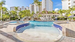 A resort with a swimming pool, palm trees, and a waterfall. - Luxurious condo with on-site pool, private extended balcony, & W/D (Naples)