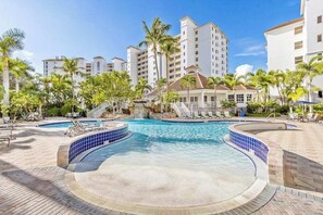 A resort with a swimming pool, palm trees, and a waterfall. - Luxurious condo with on-site pool, private extended balcony, & W/D (Naples)