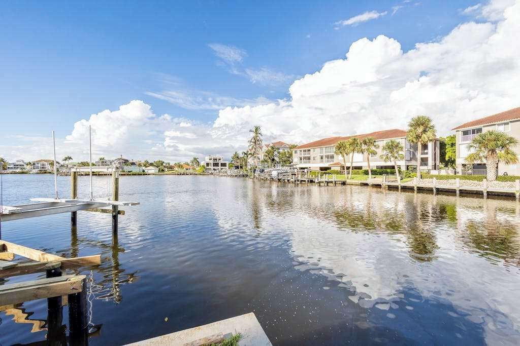 A marina with docked boats, a calm water body, and buildings with a uniform architectural style in the background.