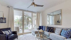A living room with a sofa, a glass coffee table, a black leather armchair, and a large mirror. - Luxurious condo with on-site pool, private extended balcony, & W/D (Naples)
