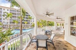 A hotel balcony with a pool, palm trees, and outdoor seating. - Luxurious condo with on-site pool, private extended balcony, & W/D (Naples)