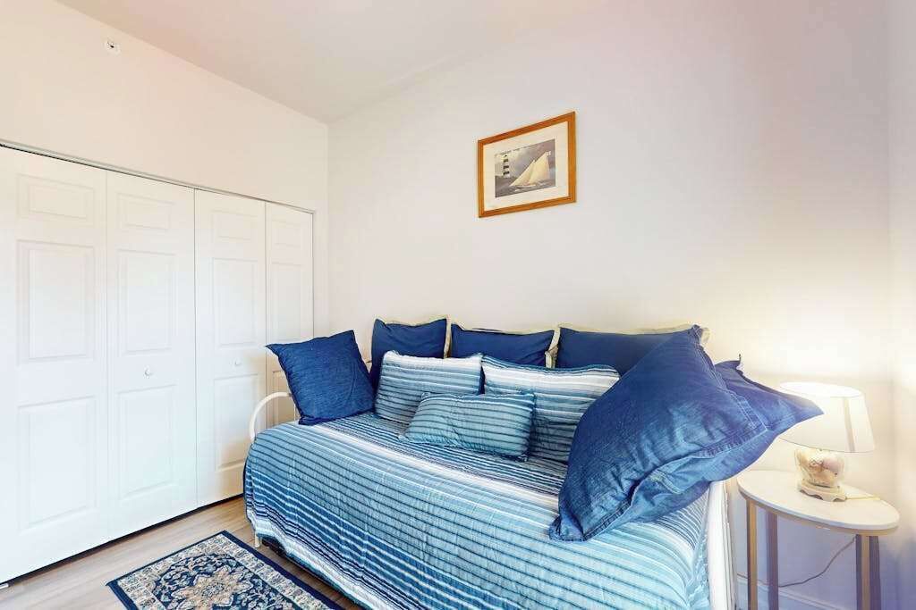 Ein Schlafzimmer mit einem Bett, einem weißen Kleiderschrank, einem gerahmten Bild an der Wand und einem Nachttisch mit einer Lampe.