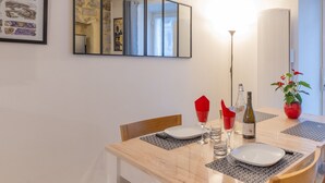 Uma área de refeições com uma mesa posta para dois, uma garrafa de vinho e um vaso com planta.