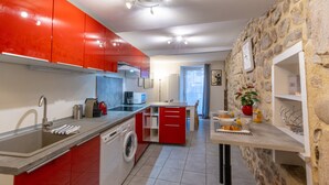 Uma cozinha moderna com armários vermelhos, uma máquina de lavar e uma área de jantar com parede de pedra.