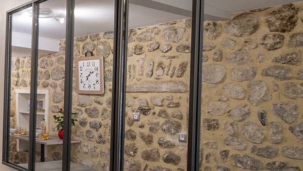 Paredes de pedra com um relógio, uma porta de vidro e uma área de refeições com mesa e cadeiras.