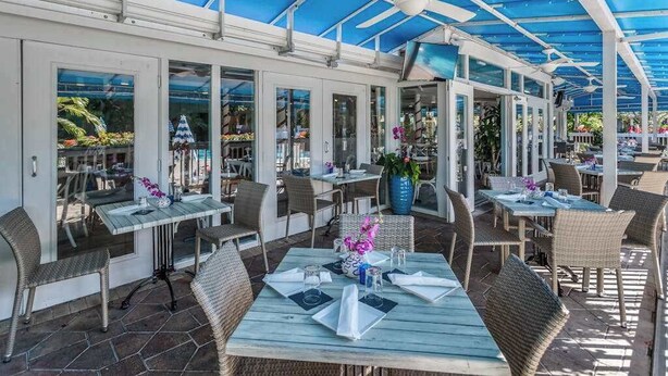 Un espace de restauration en plein air, doté de tables et de chaises, d’un toit abrité et de grandes fenêtres.