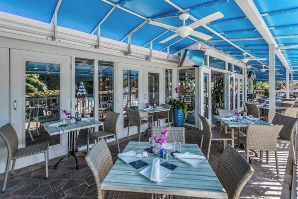 An outdoor dining area with tables and chairs, a covered ceiling, and large windows. - Water view condo with WiFi, screened balcony, pool, tennis, & on-site dining (Naples)