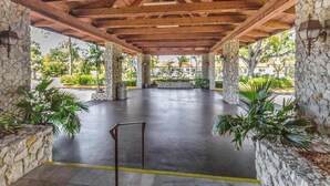 Un espace extérieur abrité, doté de piliers en pierre, d’un sol en béton et de plantes en pot.
