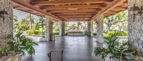 A covered outdoor area with stone pillars, a flat concrete floor, and potted plants.