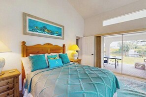 A bedroom with a bed, a nightstand, a lamp, a painting, and a sliding glass door leading to an outdoor area. - Relax, Recharge & Explore. Your Waterfront Getaway Awaits. (Punta Gorda)