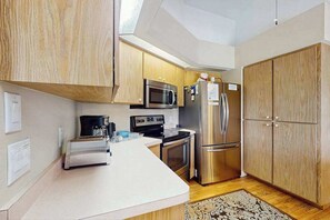 A compact kitchen with wooden cabinets, a stainless steel refrigerator, a microwave, and a coffee maker. - Relax, Recharge & Explore. Your Waterfront Getaway Awaits. (Punta Gorda)