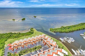 Vista aérea de un hotel con estacionamiento, un puerto deportivo con barcos y una gran masa de agua.
