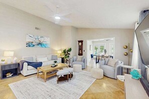 Un salon avec un canapé, des poufs, une table basse et un tableau accroché au mur.