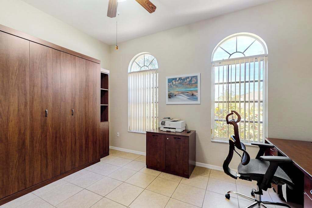 Una habitación con un armario grande, un escritorio con silla, una impresora y dos ventanas con persianas.