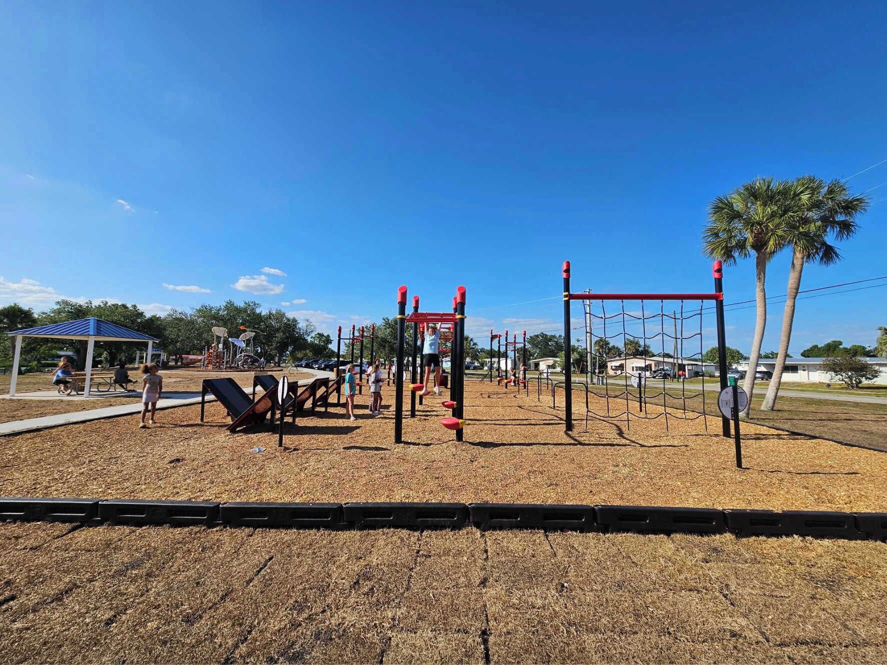 Un parque infantil con diversas estructuras de juego, una zona de estar cubierta y un cielo despejado.