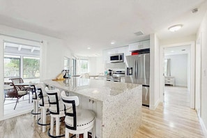 A modern kitchen with a large island, bar stools, stainless steel appliances, and a view of the outdoors. - Relax in Style home screened porch, WiFi, in-unit washer/dryer (Naples)