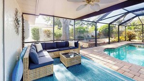 A sunlit indoor pool area with a sofa and coffee table, large windows, and a ceiling fan. - Contemporary and cozy home with heated pool, central location, close to beaches (Naples)