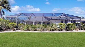 Een huis met een overdekte patio, omgeven door een verzorgd gazon en diverse struiken.