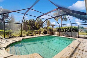 A swimming pool with a glass enclosure, surrounded by a brick patio and palm trees. - Sunny Snowbird Retreat with a Pool, Furnished Lanai, & Prime Corner Lot (Port Charlotte)