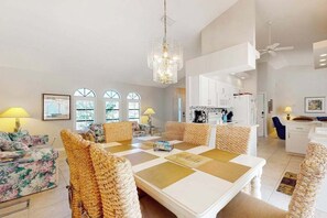 A spacious living room with a dining area, large windows, and a kitchen in the background. - Sunny Snowbird Retreat with a Pool, Furnished Lanai, & Prime Corner Lot (Port Charlotte)