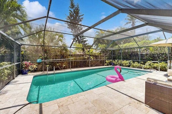 Ein überdachter Pool mit einem rosa Flamingo-Schwimmtier, umgeben von Pflanzen und Bäumen.