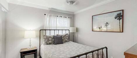 Un dormitorio con cama, lámparas de noche, mesita de noche, ventilador de techo y un cuadro enmarcado en la pared.