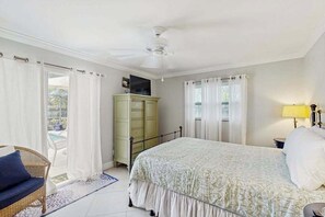 Ein Schlafzimmer mit Bett, Kommode, Fernseher und einem Fenster mit Vorhängen.