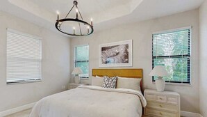 Une chambre à coucher avec un lit, des tables de chevet, un lustre et un tableau encadré au mur.