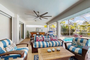 A sunlit room with wicker furniture, a ceiling fan, and a view of a pool. - Waterfront home with private, heated pool, dock, and lanai (Cape Coral)