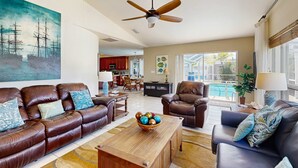 Ein geräumiges Wohnzimmer mit Ledersofas, einem Holztisch und einem Deckenventilator.