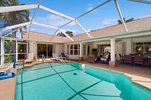 A pool area with a covered section, lounge chairs, and a patio with outdoor furniture. - Waterfront home with private, heated pool, dock, and lanai (Cape Coral)
