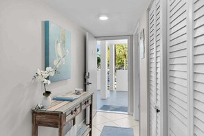 A hallway with a wooden console table, a vase with white flowers, and a painting on the wall. - Water view condo with shared pool, panoramic balcony views, and WIFI (Marco Island)